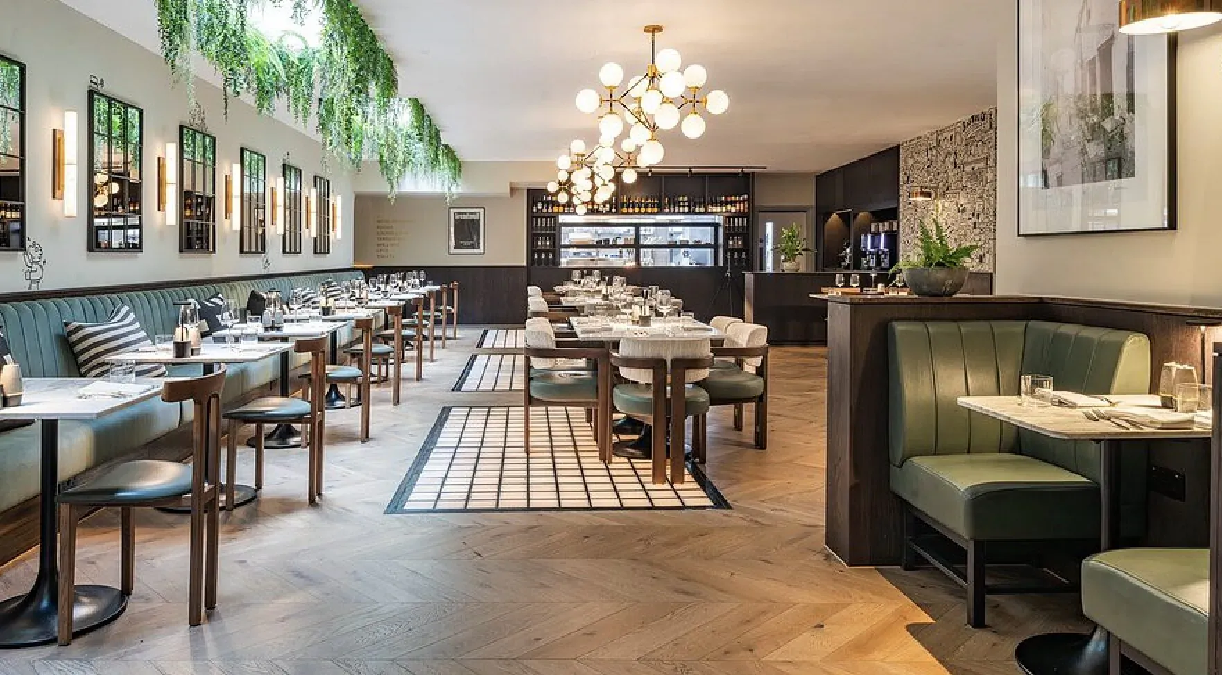 Elegant dining room at Treadwell Restaurant, Oxford, with wooden tables, green banquettes, pendant lights, and hanging plants.
