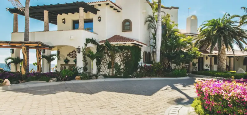 Luxurious white Spanish-style villa with palm trees, lush gardens, pink flowers, and ocean view