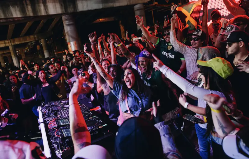 Crowd cheers with arms raised at Boiler Room DJ set in Miami club under neon lights, Jamaican flags waving.