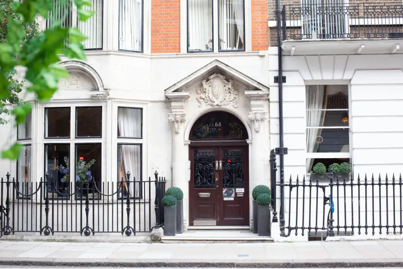 Elegant Victorian townhouse entrance with arched doorway, ornate pediment, black railings, and potted plants on London street.