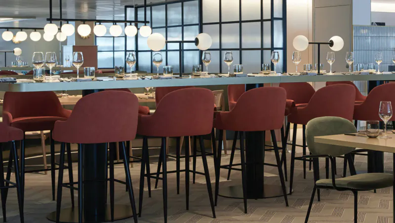 Modern Virgin Cruises bar with red upholstered stools, glassware on counter, pendant lights, and glass partition.