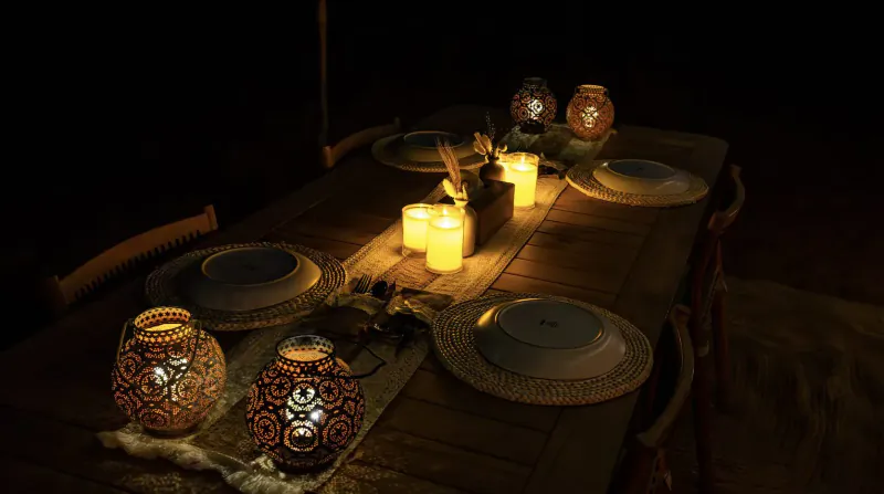 Elegant desert dining table with ornate lanterns, flickering candles, white plates, and woven runner in dim lighting