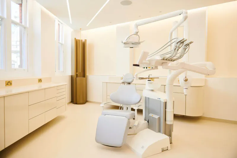 Modern empty dental chair in a bright, minimalist cosmetic dentistry clinic with sleek white cabinetry and lighting.