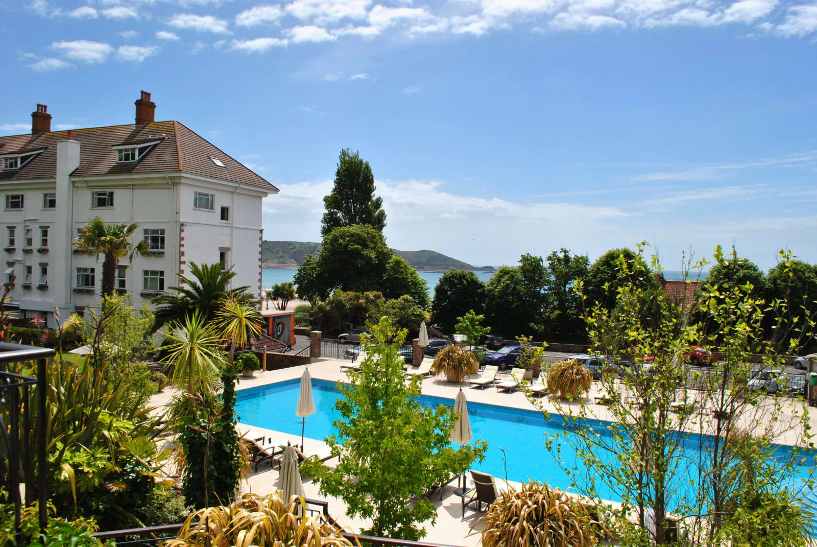 St. Brelade’s Bay Hotel in Jersey: outdoor pool with white umbrellas, palm trees, gardens, and sea view.