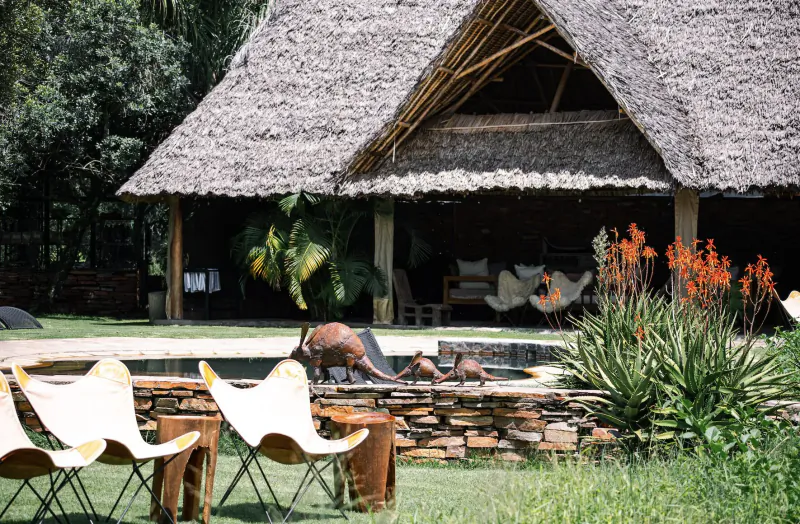 White butterfly chairs by infinity pool with giraffe sculpture at thatched House In The Wild lodge, Kenya, surrounded by lush greenery