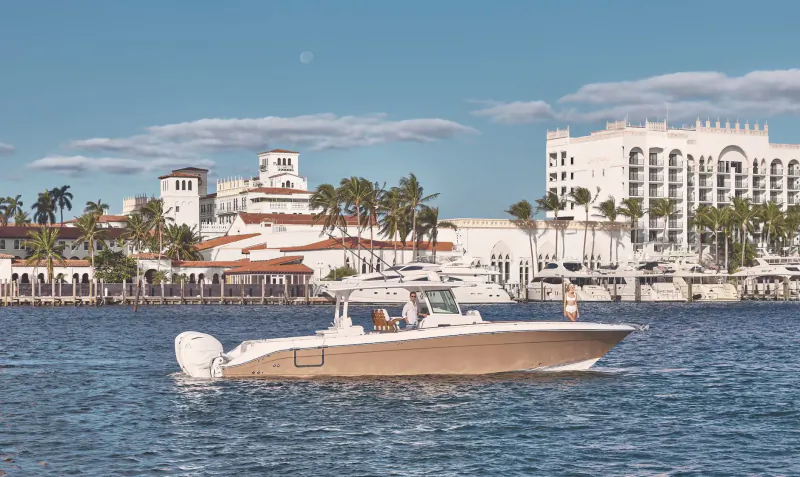 Tan speedboat with captain cruising turquoise waters near white luxury hotels and palms in Palm Beaches.