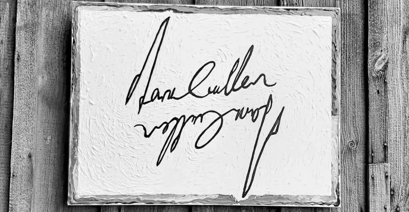 Black and white photo of 'Dan Cullen' signature on white canvas in rustic wood frame on wooden wall.