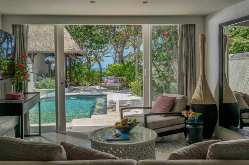 Luxurious Maldives villa interior with pool, lounge seating, tropical garden, and ocean view beyond.