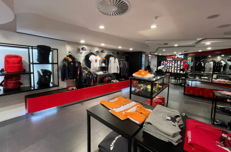 Grand Prix Store displaying red, white, orange racing apparel, helmets, bags on racks and shelves.