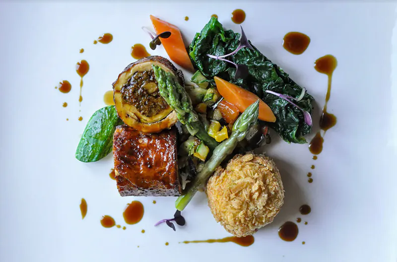 Elegant plated dish: glazed meat roll, asparagus, carrots, kale, croquette, balsamic sauce on white plate