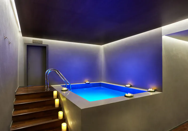 Small glowing blue pool with candles at Naturelife Spa, wooden steps and ambient lighting