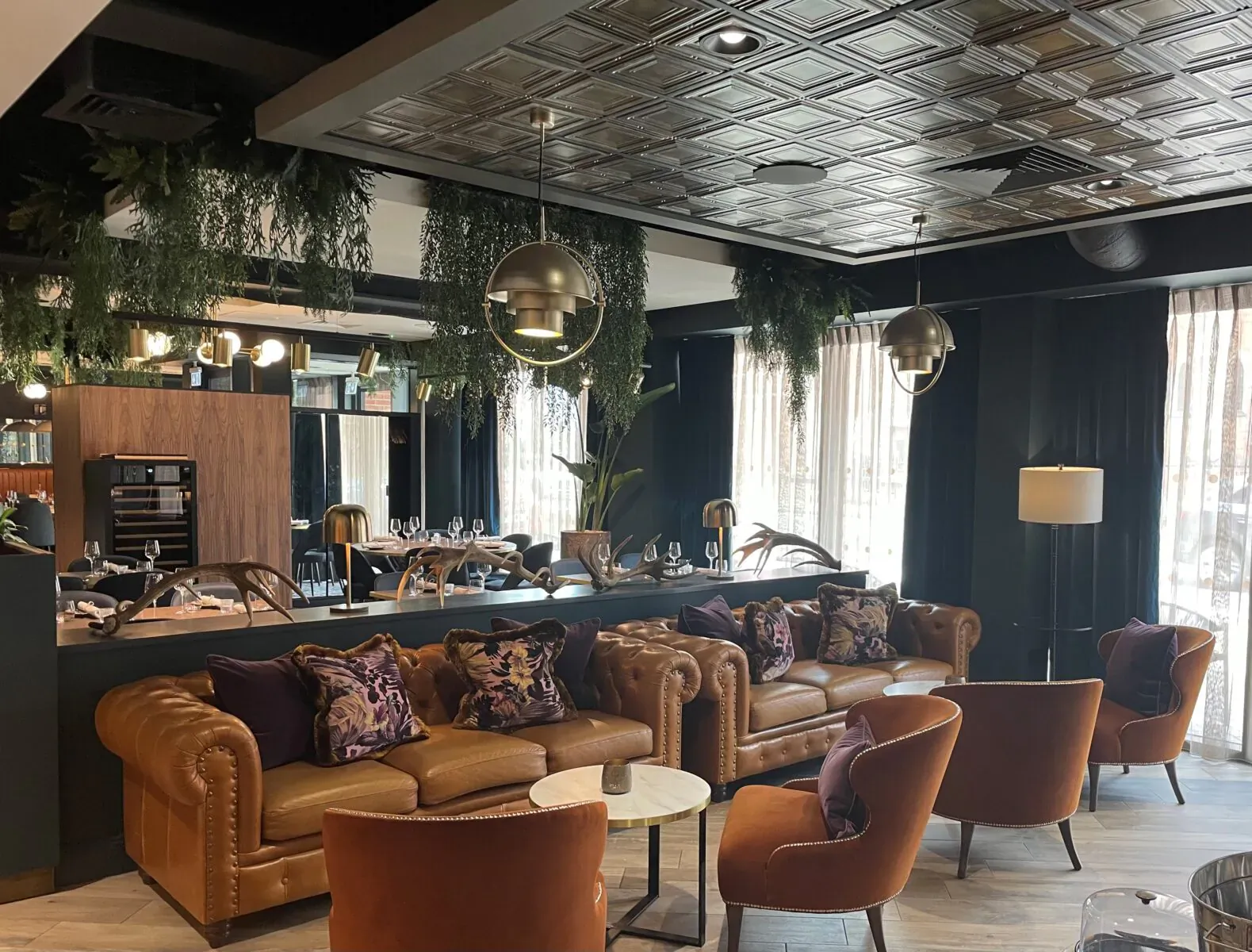 The Forge lounge at Hotel Indigo Chester: leather sofas, purple cushions, bar counter, pendant lights, plants, tin ceiling.
