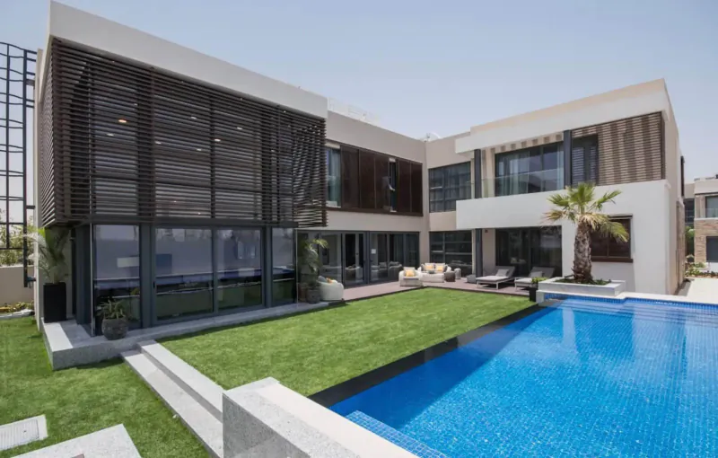 Modern Dubai luxury villa with wooden screens, glass walls, lush lawn, palm trees, outdoor seating, and infinity pool.
