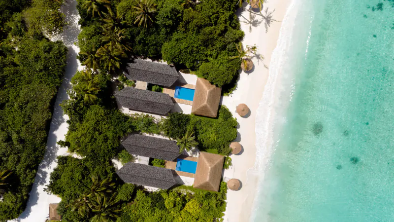 Aerial view of RAAYA by Atmosphere luxury thatched villas with blue pools amid lush greenery and turquoise Maldives beach