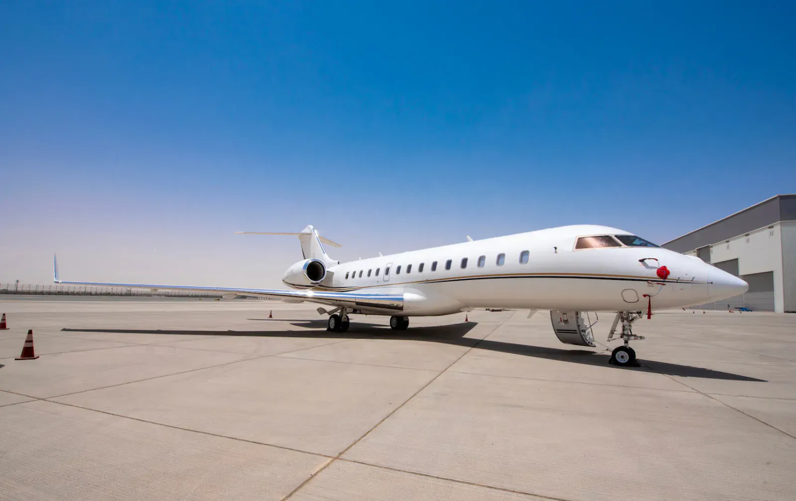 White JETLUXE private jet parked on tarmac near hangar under clear blue sky with traffic cones.