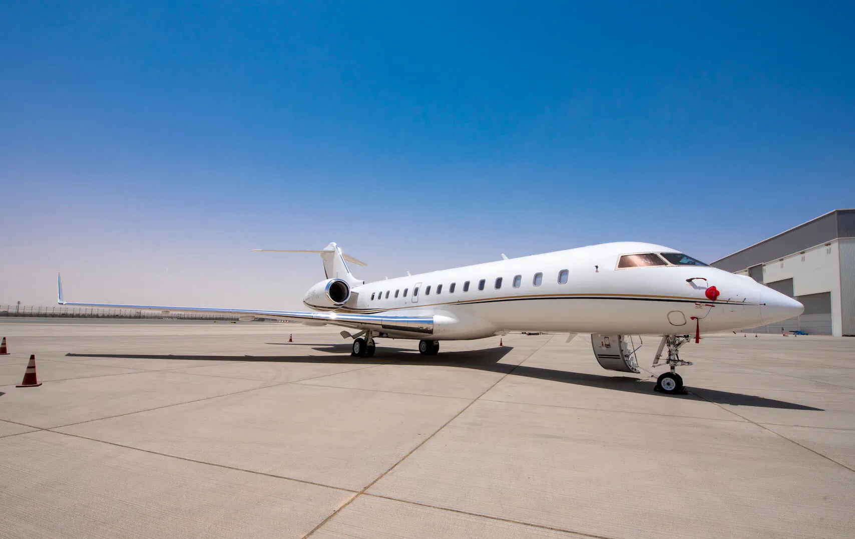 White JETLUXE private jet parked on tarmac near hangar under clear blue sky with traffic cones.