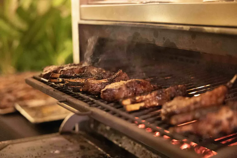 Grilled ribs on smoky barbecue grill with glowing coals and tropical plants nearby