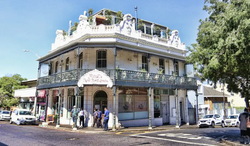 Ornate two-story corner building on Kloof Street, Cape Town, with 'Lady Ann' sign, rooftop plants, balcony, and people outside.