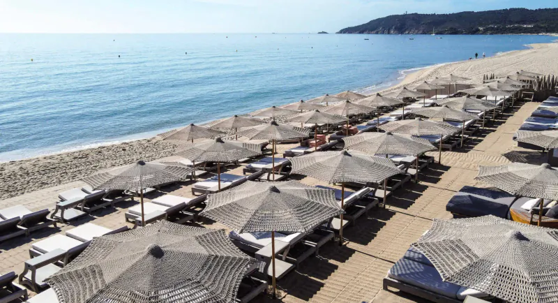 Aerial view of luxury beach at Byblos Palace hotel in Saint-Tropez with rows of straw umbrellas and loungers by the sea.