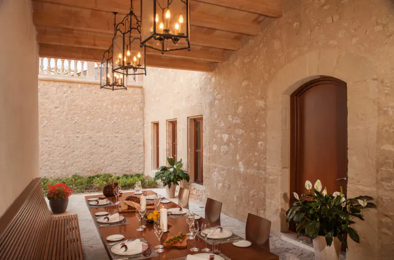 Elegant outdoor dining terrace at Castell Son Claret, Mallorca, with long set table, lanterns, plants, and stone arches.