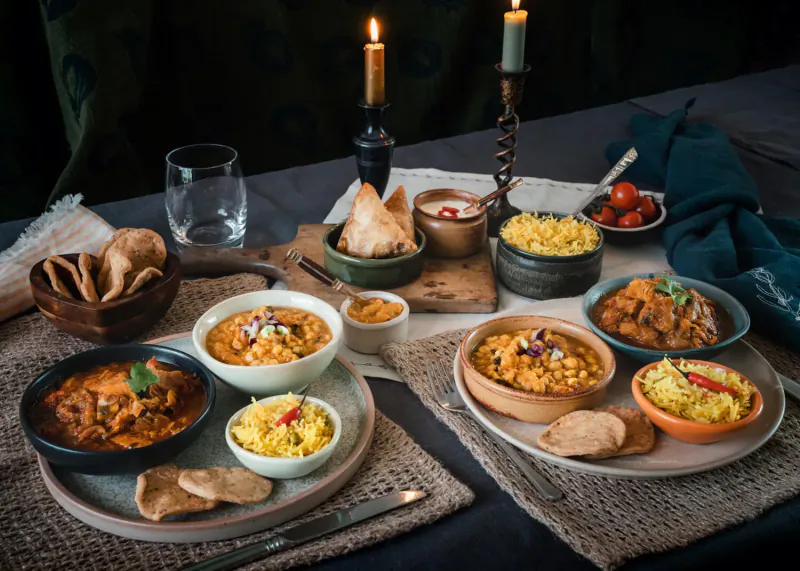 Assortment of award-winning Indian dishes like curries, rice, naan on table with candles.