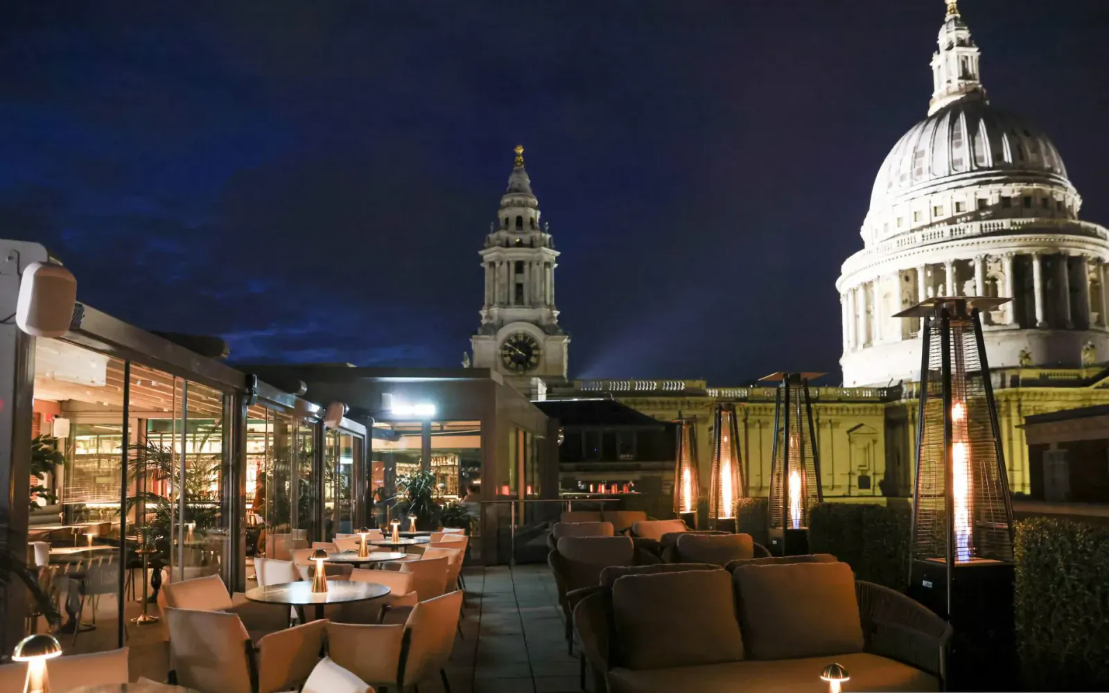 Evening rooftop terrace with tables, chairs, heaters, and London skyline featuring St. Paul's Cathedral.