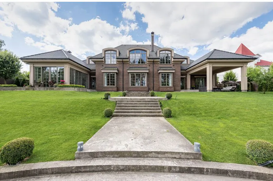 Luxury brick mansion with arched windows, covered porch, and wide stone steps on lush green lawn