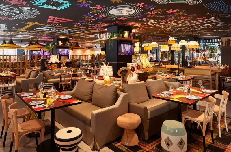 Vibrant Mama Shelter restaurant in East London with eclectic decor, colorful ceiling art, lamps, plush sofas, and dining tables.