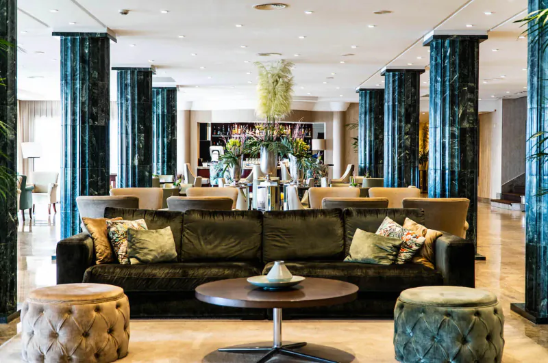 Luxurious hotel lobby with green marble columns, plush green sofas, coffee table, and floral arrangements.