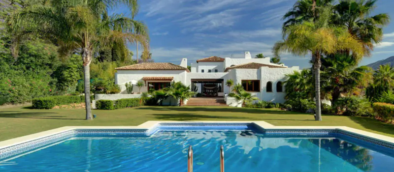 Luxury white villa with terracotta roof, infinity pool, palms, and mountain backdrop in Marbella