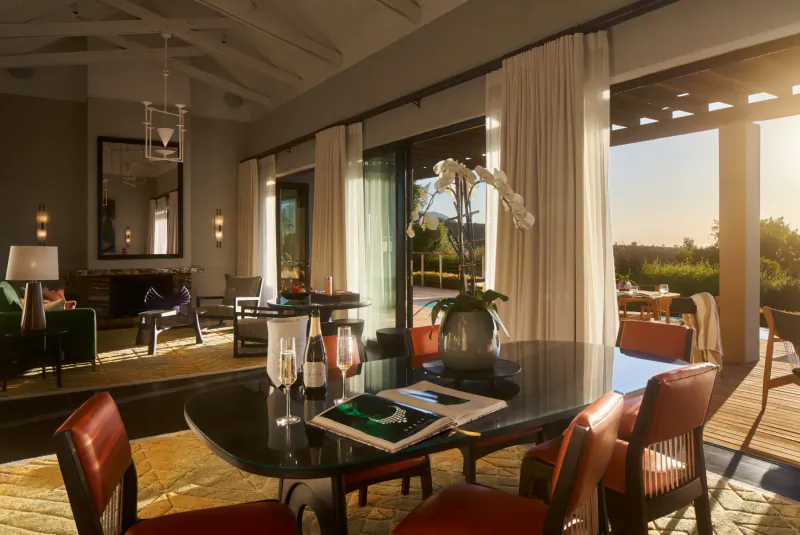 Luxurious Delaire Graff Estate dining area with table set for wine, orchids, pool, and Cape Winelands sunset view.