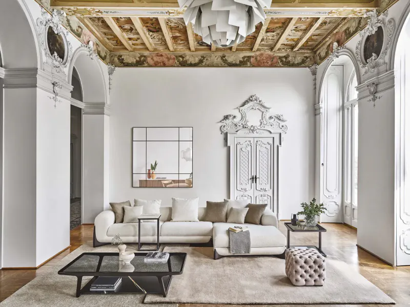 Elegant living room with white L-shaped sofa, glass coffee table, ornate double doors, gilded ceiling, and arched windows.