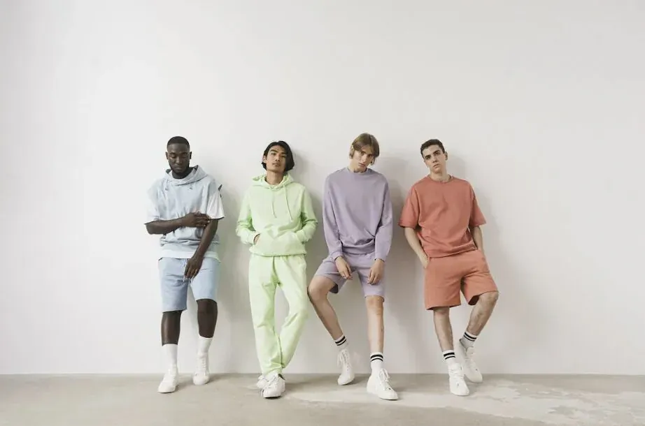 Four diverse men posing in colorful athleisure tracksuits against white wall: blue, lime green, purple, orange.