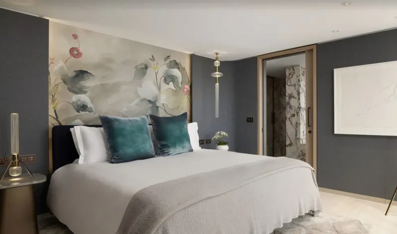 Luxurious hotel bedroom with gray walls, floral wallpaper headboard, teal pillows, white bedding, gold lamps, and open door.