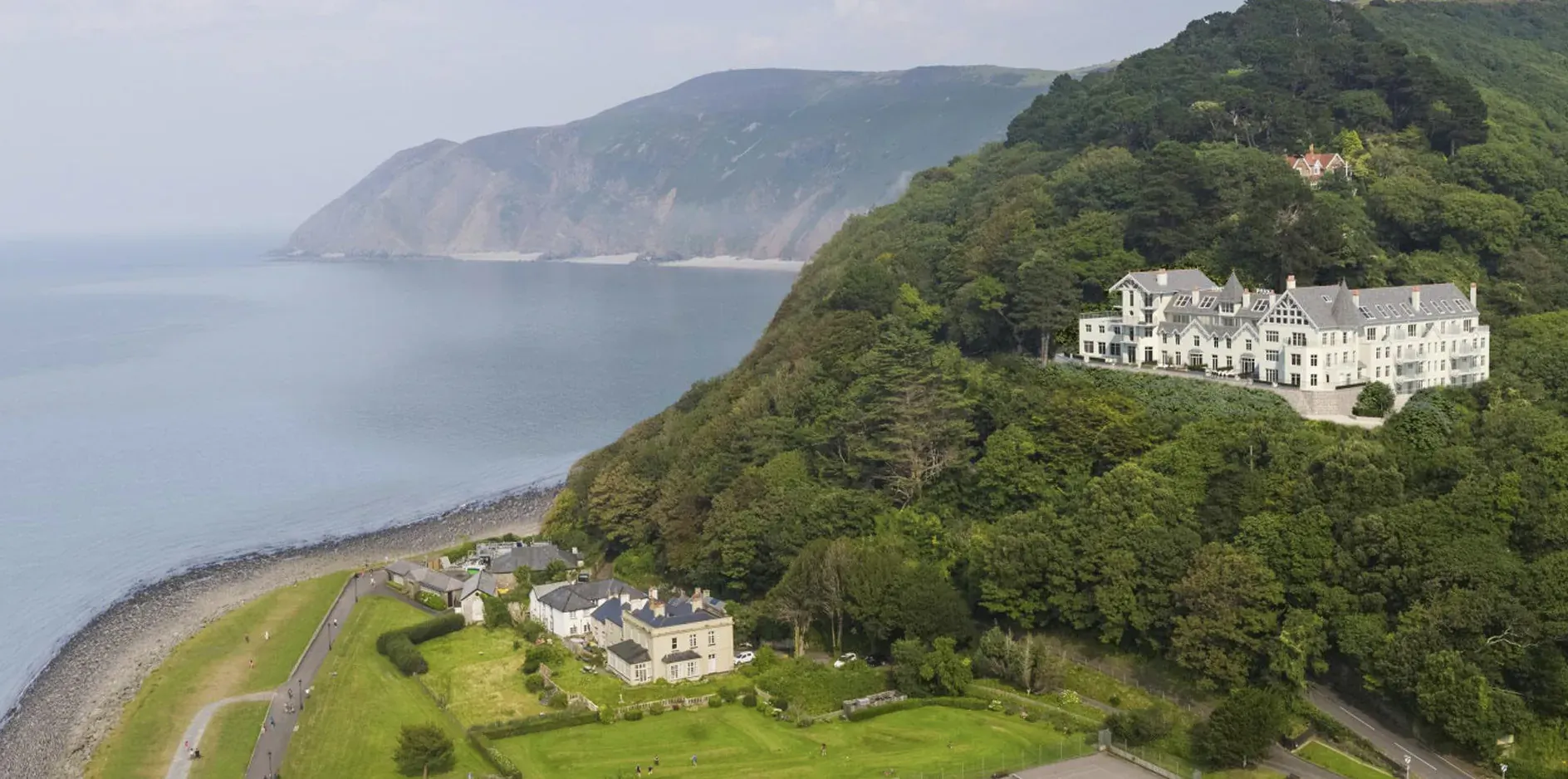Tors Park manor nestles on green hill against rugged Exmoor coastline in Devon, aerial view.