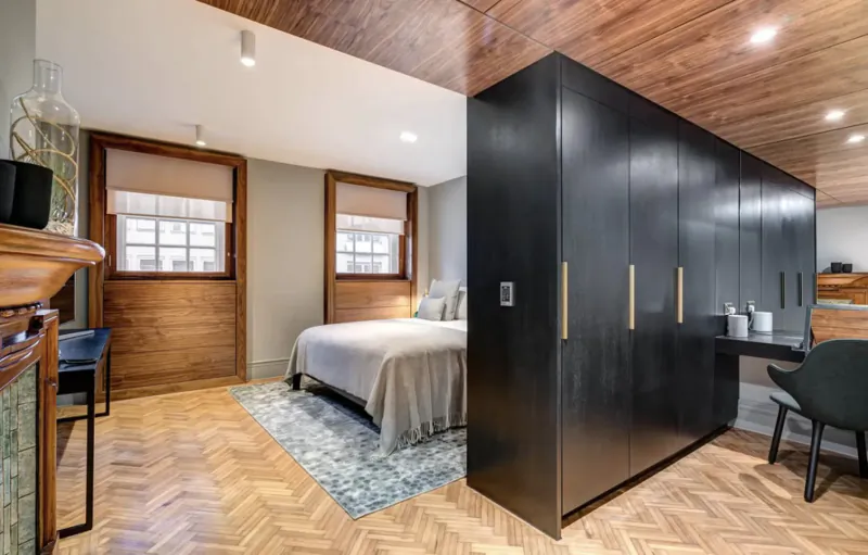 Cozy modern hotel bedroom at Apex Temple Court with wooden accents, king bed, black wardrobe, desk, and windows.