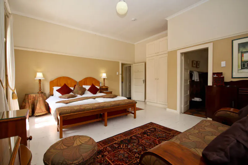 Elegant hotel bedroom at Montagu Country Hotel with wooden king bed, cream walls, Persian rug, and armchair.