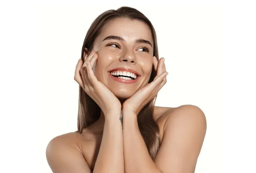 Smiling woman with radiant skin cups face with hands, showcasing bright future smile on white background