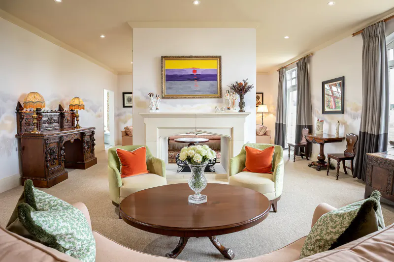 Elegant luxury manor home living room with green armchairs, round wood table, fireplace, and abstract yellow-purple painting.