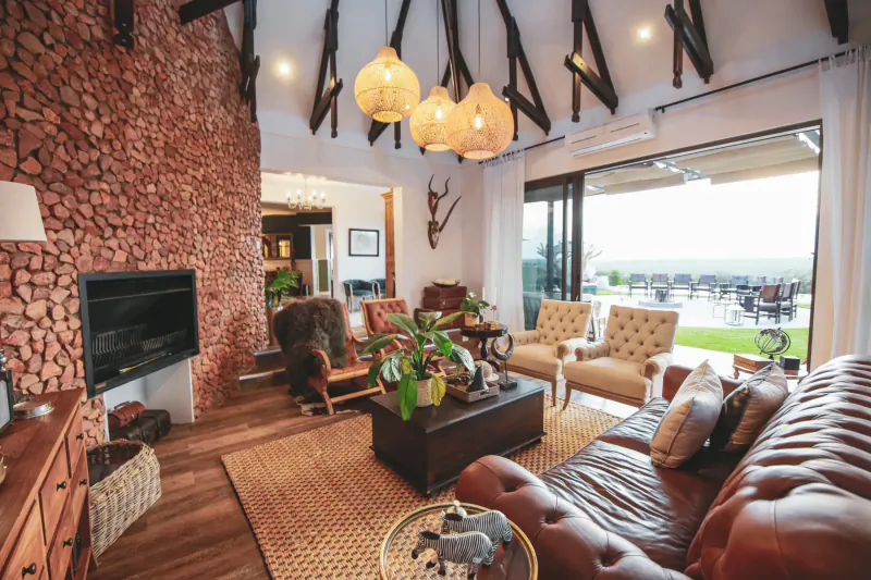 Spacious Namibian living room with red brick fireplace, leather sofa, antler decor, plants, and pool view.