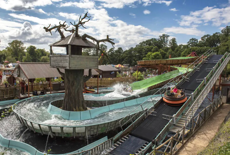 Treehouse with twisting blue water slide and green flume at safari park lodges, bumper boats on track nearby