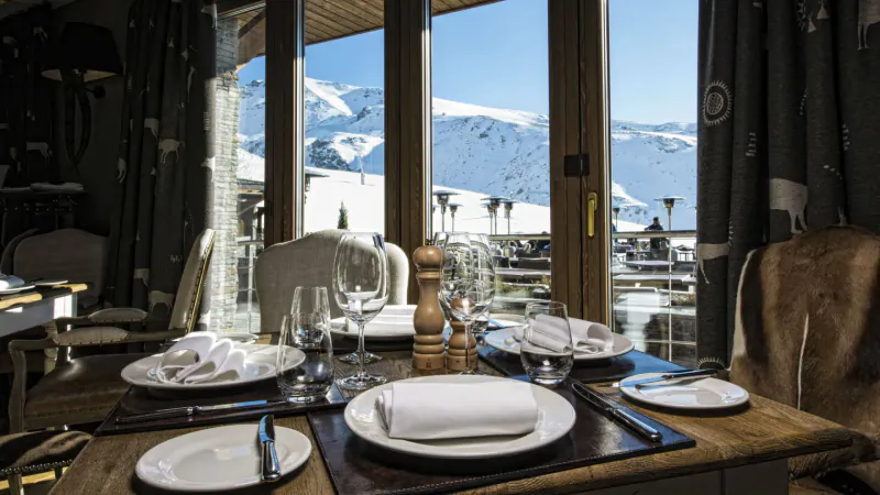 Elegant dining table set with white plates and wine glasses at El Lodge, Sierra Nevada, with snowy mountain view.