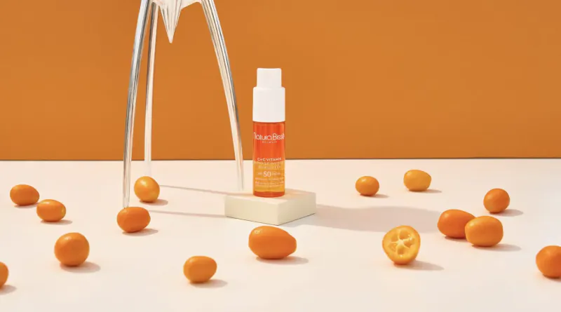 Natura Bissé orange sun protection spray bottle on white stand amid kumquats, orange background