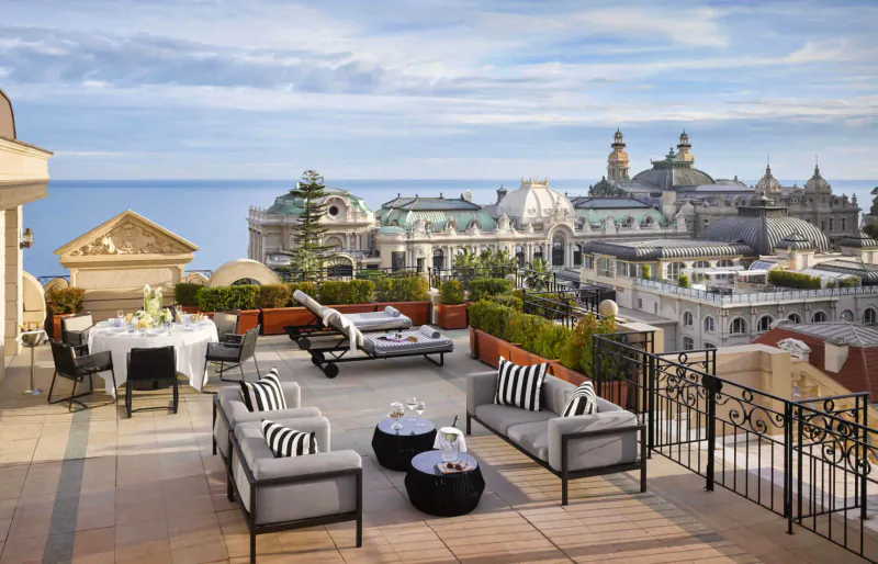 Hotel Metropole Monte-Carlo rooftop terrace with lounge seating, dining table, and panoramic view of Casino gardens and sea.