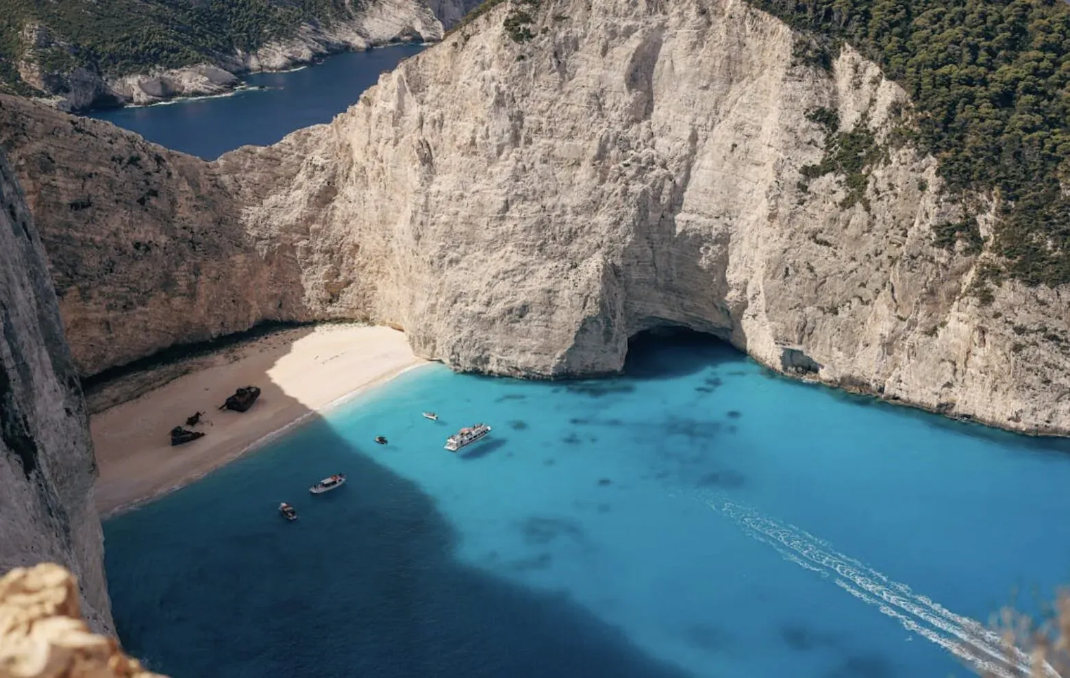 Aerial view of Navagio Beach, Zakynthos: white sand cove, turquoise waters, towering cliffs, boats on sea.