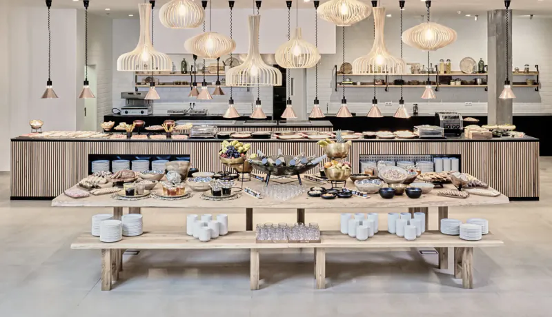 Elegant hotel buffet at Baobab Suites resort with white bowls, pastries, and pendant lights over wooden counters.