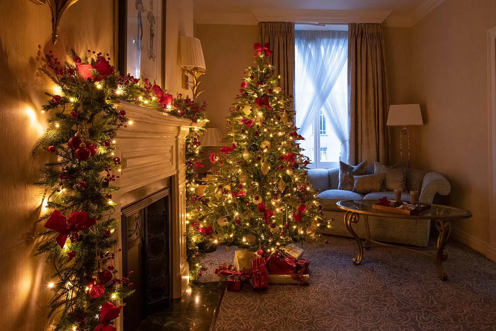Luxurious hotel room with lit Christmas tree, garlanded fireplace, and presents in The Landmark London.