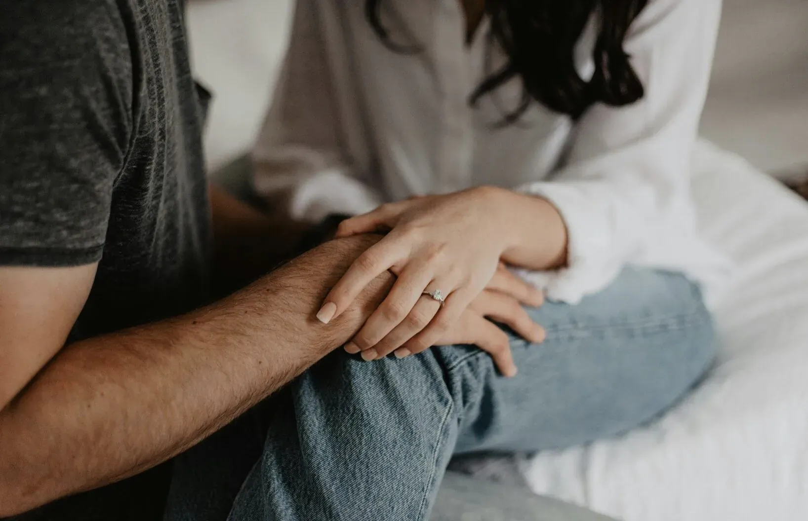 Close-up of couple's hands intertwined on bed, woman's ring visible, symbolizing support