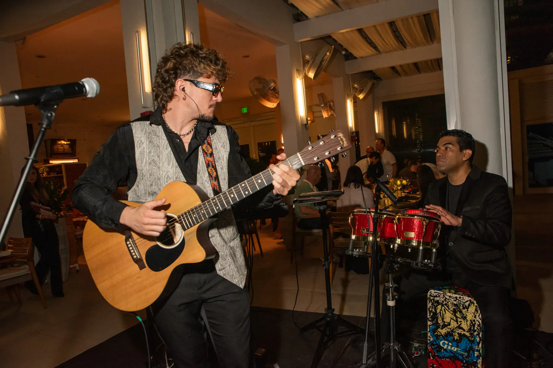 Pat Martin with shaggy hair and shades strums acoustic guitar on stage with drummer at food festival