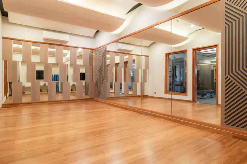 Spacious modern gym with wooden floors, full-length mirrors, and geometric wall panels at Hideaway Beach Resort & Spa